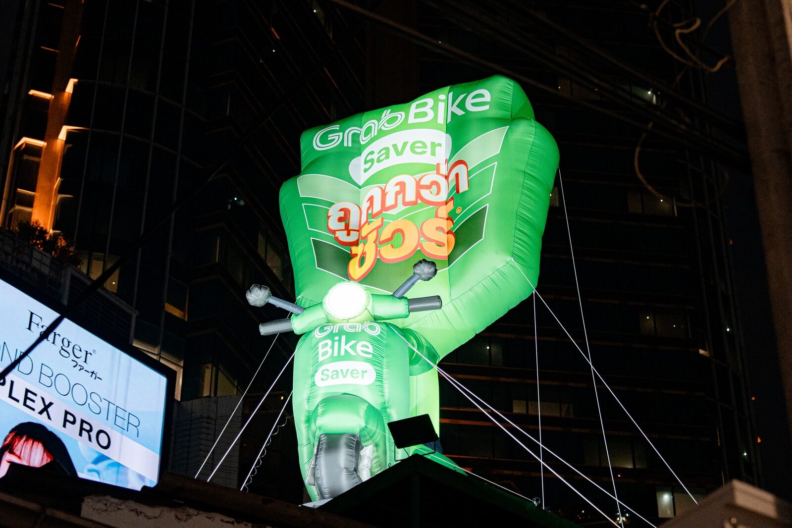Giant glowing green GrabBike inflatable scooter mounted above a night street