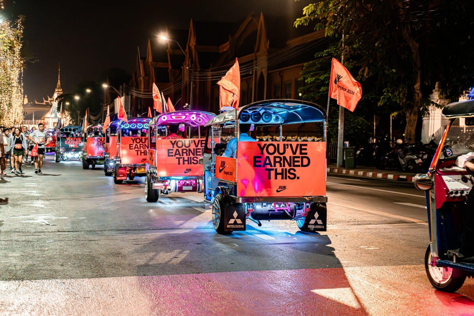 Convoy of Nike YOU'VE EARNED THIS tuk-tuks glowing with neon on a Bangkok street at night