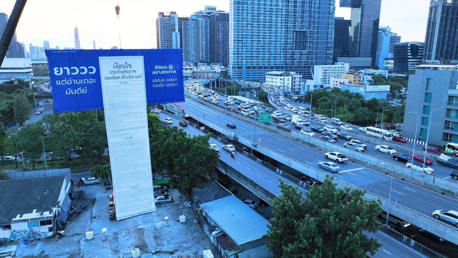 Allianz Ayudhya giant vertical tower banner over a Bangkok expressway at dusk