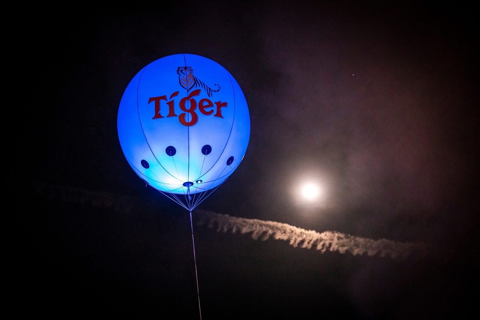 Illuminated blue Tiger balloon floating beside a full moon at night