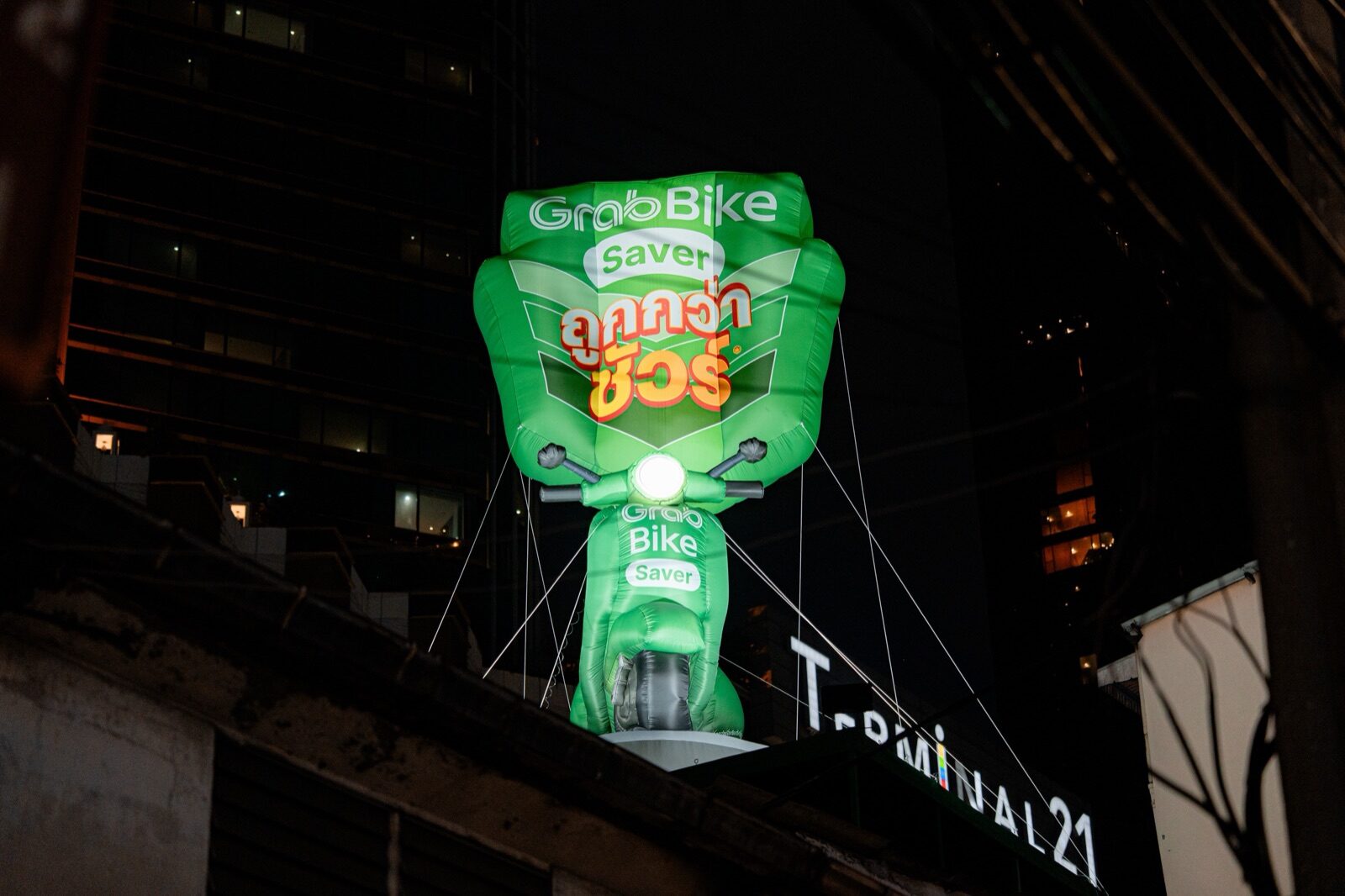Giant green GrabBike Saver inflatable scooter mounted on Terminal 21 at night