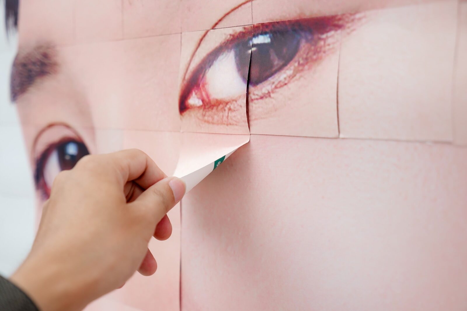 Hand peeling a giant pasted street poster of a woman's eye